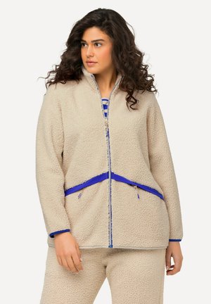 Veste en polaire beige avec des accents bleus, dotée d'une fermeture éclair, de poches latérales et d'une surface douce et texturée. Assortie avec un pantalon correspondant.
