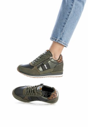 Zapatillas verdes con una mezcla de texturas mates y brillantes, con detalles en negro, un cierre y un tacón estampado. Suela plana de goma.