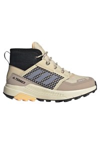 Zapato de exterior de corte medio en color beige y negro, con detalles de malla, suela de goma y distintivo logo de tres franjas en el costado.