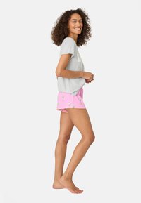 Grå kortärmad T-shirt med lös passform, kombinerad med rosa shorts med ett mönster av cocktailglas. Modellen står barfota och ler.