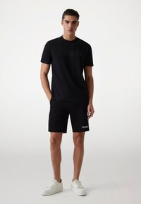 Czarna koszulka z wytłoczonym logo "GUESS", zestawiona z czarnymi szortami z białym nadrukiem "GUESS". Wykończona białymi trampkami.