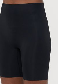 Sorte høy midje shorts laget av glatt stoff, med en tett passform og subtile sømdetaljer langs sømmene.