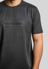 Zwart T-shirt met korte mouwen van gladde stof, met een gestructureerd rechthoekig logo "PEUTEREY" op de borst. Eenvoudig ontwerp, geen patronen.