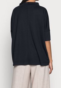 Marinblå oversized topp med bred rundad hals, korta ärmar och mjuk textur, kombinerad med ljusbeige vida byxor.