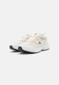 Bijele i breskvaste atletske tenisice s mrežastim panelima, teksturiranim preklopima i crnom gumenom potplatom. Imaju logo na jeziku i sa strane.