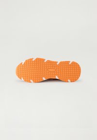 Sport shoe outsole with a textured orange rubber pattern, white accents, and visible tread. Designed for grip and durability.