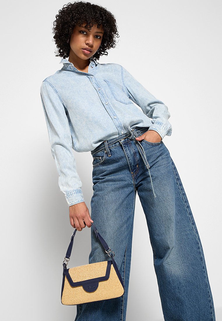 Camicia di jeans blu chiaro con bottoni e taschino; jeans blu a gamba larga; piccola borsa intrecciata gialla con dettagli blu marino e manico.