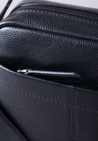 Black leather bag with a textured surface, featuring a zipper closure and a small front pocket. Visible stitching adds detail.