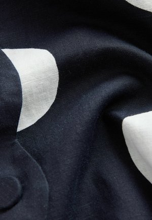 Tessuto di cotone con uno sfondo blu navy e grandi forme astratte bianche. Superficie strutturata con leggere pieghe, che enfatizzano la morbidezza del materiale.