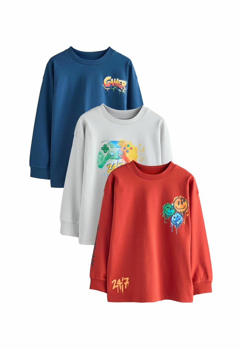 Tres camisetas de manga larga: azul con el gráfico "GAMER", gris con un diseño de controlador de juegos y roja con acentos de carita sonriente. Material de algodón suave.