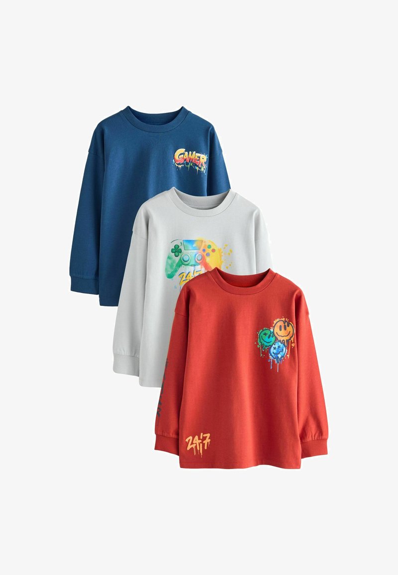 Tres camisetas de manga larga: azul con el gráfico "GAMER", gris con un diseño de controlador de juegos y roja con acentos de carita sonriente. Material de algodón suave.