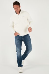 Valge poolpusa, millel on poole viskiga krae, rinnal tikitud logo, koos keskmise sinise kulunud teksapükste ja valgete tossudega.