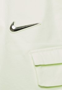 Jasnozielony materiał o teksturowanym wykończeniu, z logo Nike w kolorze srebrnym oraz małą kieszonką na klapę.