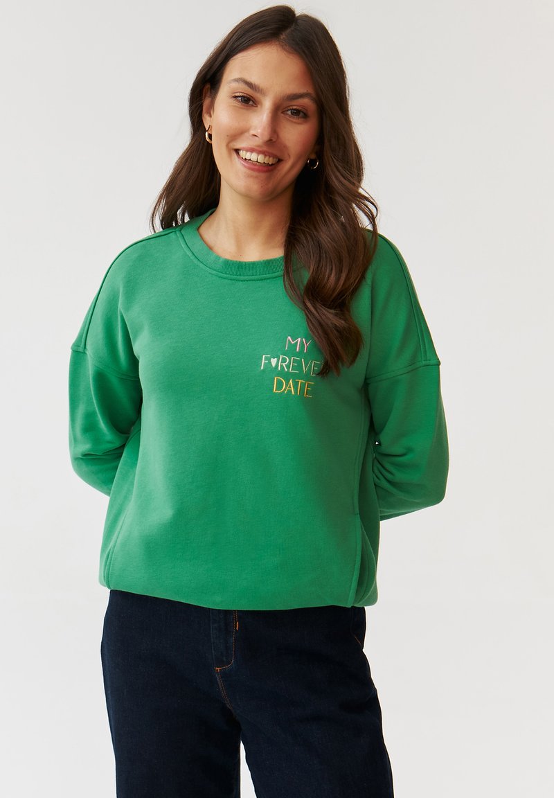 Zielona bluza z okrągłym dekoltem, opuszczonymi ramionami i haftowanym napisem "MOJA NA ZAWSZE RANDKA" w kolorze różowym i żółtym. Miękka tkanina, luźny krój.