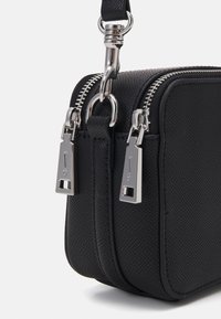 Čierna textúrovaná kožená crossbody taška s duálnymi striebornými zipsami a obdĺžnikovými úchytkami, s nastaviteľným popruhom. Kompaktný obdĺžnikový tvar.