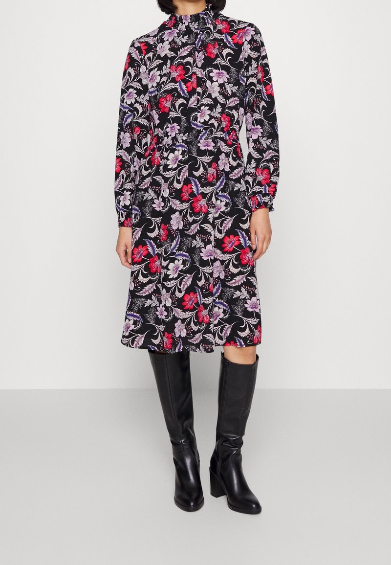 Šaty s dlouhými rukávy s černým pozadím a květinovými vzory v červené, fialové a bílé barvě. Upravené v pase, s vysokým límcem.