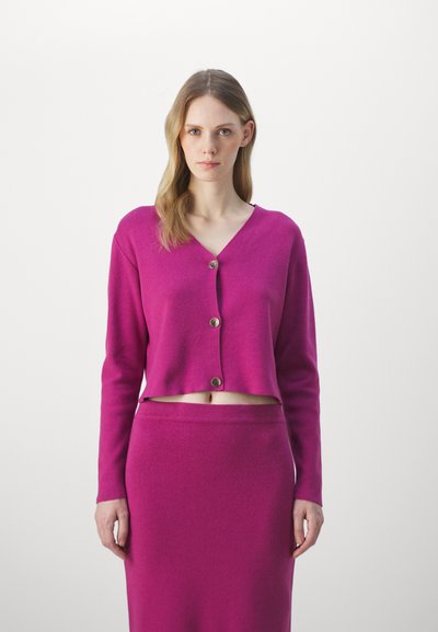 Fuchsia gestrickte Strickjacke mit V-Ausschnitt, verkürztem Schnitt und vorderen Knöpfen, kombiniert mit einem passenden fuchsia farbenen Rock. Glatte Textur, einfaches Design.