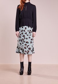 Svart långärmad topp med ett nyckelhålsdetalj, matchad med en ljusblå blommönstrad kjol. Svarta platå stövletter avslutar looken.