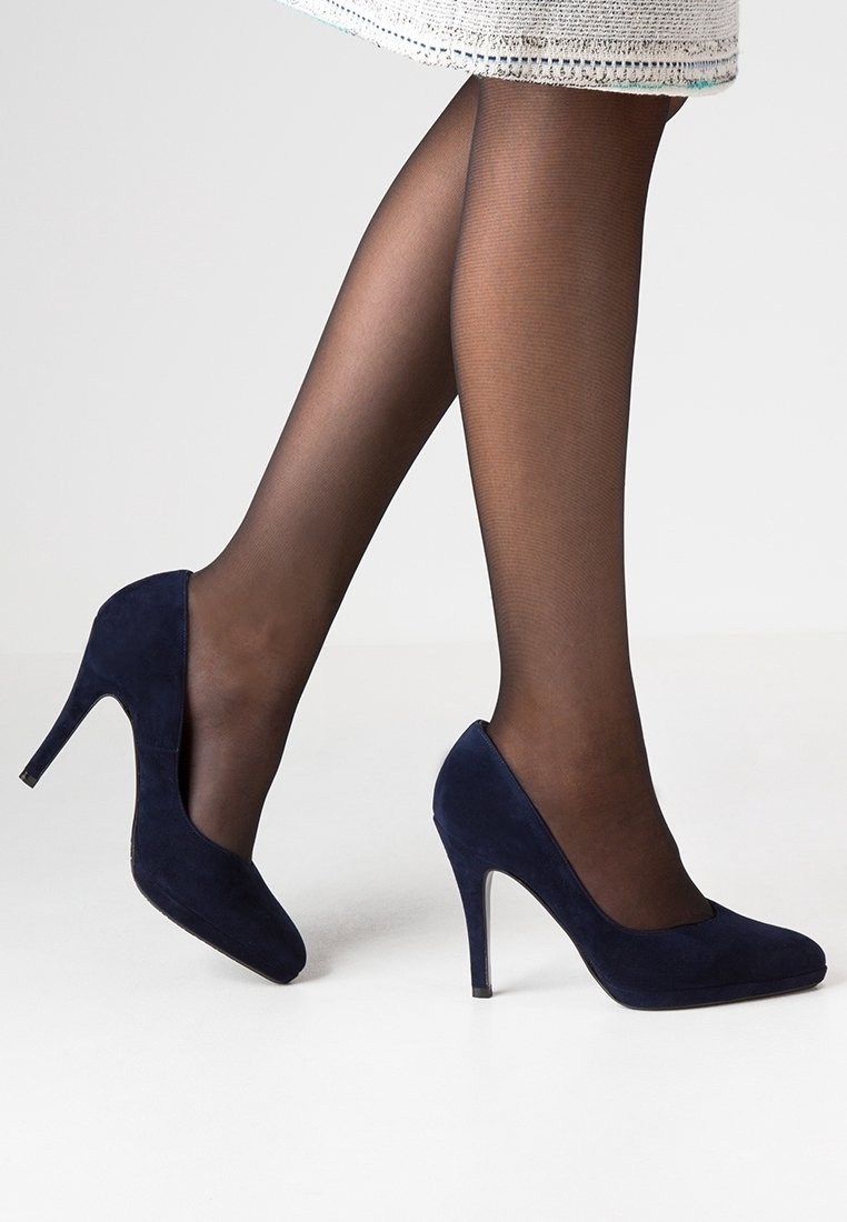 Talons hauts en suede bleu marine avec un bout pointu, un talon aiguille de 10 cm et une texture lisse, portés avec des collants noirs transparents sur un fond clair.