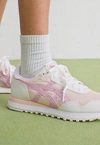 Tênis atléticos brancos e rosa com parte superior em malha e sintético, apresentando detalhes em rosa e uma sola texturizada, combinados com meias cinzas em canelado.