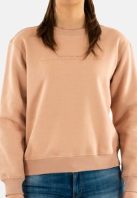 Felpa rosata con colletto a girocollo, cuciture visibili, polsini e orlo a costine, caratterizzata da un testo del logo in una tonalità leggermente più scura.