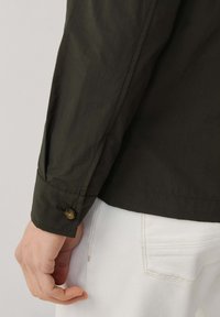 Ciemnozielona koszula zapinana na guziki z teksturowanej tkaniny, z mankietem na guzik, w połączeniu z białymi dżinsami.