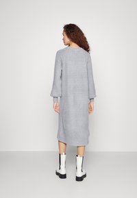 Harmaa neulottu pitkä neulemekko, jossa on ribbikuvio, tiputettu hihnat ja sivuaukot, yhdistetty mustiin ja valkoisiin nilkkabotteihin.