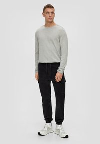 Jasnoszara koszula z długim rękawem w połączeniu z czarnymi spodniami cargo na elastycznej talii i białymi butami sportowymi z akcentem. Prosty, casualowy styl.