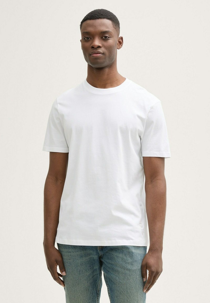 Biała koszulka z krótkim rękawem i okrągłym dekoltem, wykonana z gładkiego materiału, w zestawie z jasnoniebieskimi jeansami o luźnym kroju.