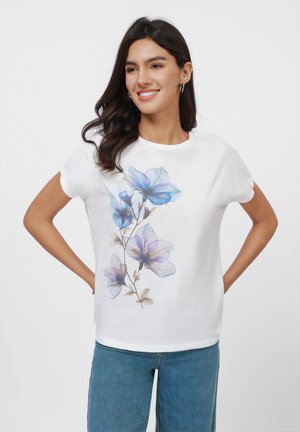 White cotton t-shirt with a floral design in blue and violet hues, featuring short sleeves and a round neckline, paired with blue jeans.