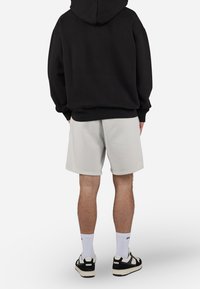 Sweat à capuche noir, shorts gris clair, chaussettes blanches, baskets noires et blanches. Matière en coton avec poignets et ourlet côtelés.