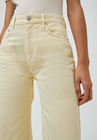 Helle gelbe Denim-Hosen mit hoher Taille, Fronttaschen und einem einzigen Metallknopfverschluss. Weicher Stoff und gerade Passform.