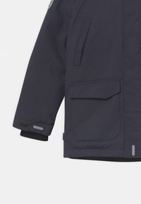 Granatowa wodoodporna kurtka zewnętrzna z kieszenią, regulowanymi mankietami i odblaskowymi akcentami. Miękki, teksturowany materiał o nowoczesnym kroju.