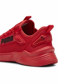 Bottine de sport rouge avec dessus en maille, superpositions texturées, talon rembourré et logo sur le côté ; dotée d'une semelle épaisse en caoutchouc avec des rainures.