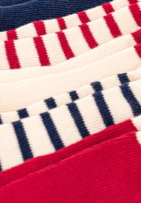 Calze di cotone impilate, presentanti colori rosso, blu navy e crema con strisce orizzontali e motivi di maglia testurizzati. Presenti sottili variazioni di colore.