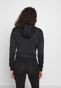 Zwarte cropped hoodie van een textuurstof, met een capuchon, lange mouwen en aansluitende boorden. Gecombineerd met zwarte leggings.