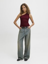 Burgundy ribbed tank top with asymmetrical cut, paired with loose, light blue denim jeans. Black textured shoes complete the outfit.
