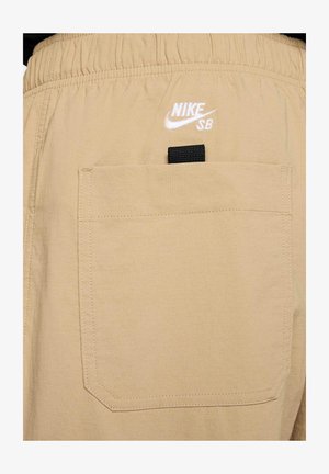 Pantaloni corti beige Nike SB con vita elasticizzata, una tasca posteriore con un'etichetta nera e logo ricamato bianco. Tessuto testurizzato.