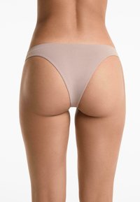 Lichtbeige thong ondergoed met een gladde textuur, minimale bedekking en een dunne tailleband, weergegeven vanuit de achterkant tegen een effen achtergrond.