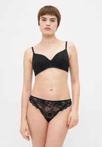 Soutien-gorge noir sans coutures avec bords festonnés et bretelles réglables, associé à un string en dentelle noire avec des motifs floraux et un bord festonné.