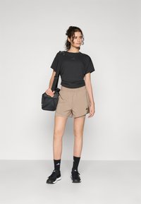 Čierne športové tričko, béžové šortky, čierne ponožky a čierne tenisky. Model má na sebe malú čiernu tašku. Jednoduchý dizajn a neutrálne farby.