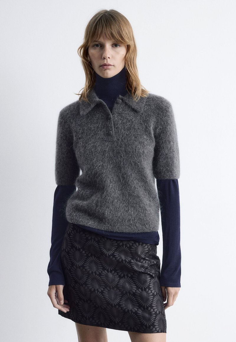 Pull court en mélange de mohair gris à col, superposé sur un haut à manches longues bleu marine, accompagné d'une mini jupe noire à motifs.