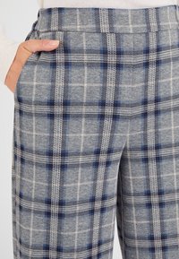 Grijze geruite broek van zachte stof, met een patroon van donkerblauwe en lichtblauwe vierkanten, voorzien van zijzakken en een gladde textuur.