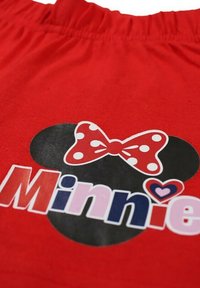 Tissu rouge avec une silhouette noire de Mickey Mouse ornée d'un nœud rouge à pois, et le mot « Minnie » en lettres colorées.
