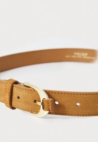 Lys brun suedesnor med spenne i gulltone i metall, med flere justeringshull og en jevn tekstur langs reimen.