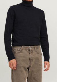 Svart polotröja av stickad tyg, med långa ärmar och slim fit, kombinerad med ljusbruna byxor med fickor.