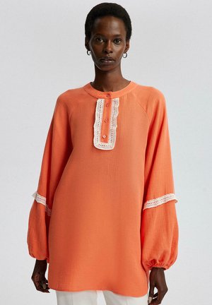Maglia arancione a maniche lunghe con scollatura arrotondata, dettagli in pizzo lungo la patta dei bottoni e ai polsini, e una vestibilità rilassata.