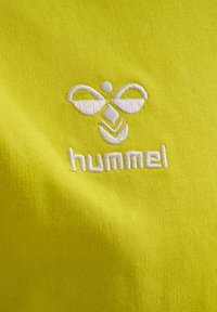 Helles gelbes Stoffmaterial mit glatter Textur, versehen mit einem weißen, gestickten Logo einer stilisierten Biene und dem darunterstehenden Wort "hummel".