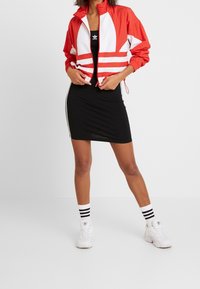 Röd och vit vindjacka med randig design, tillsammans med en svart tajt klänning. Vita sneakers och randiga strumpor fulländar looken.