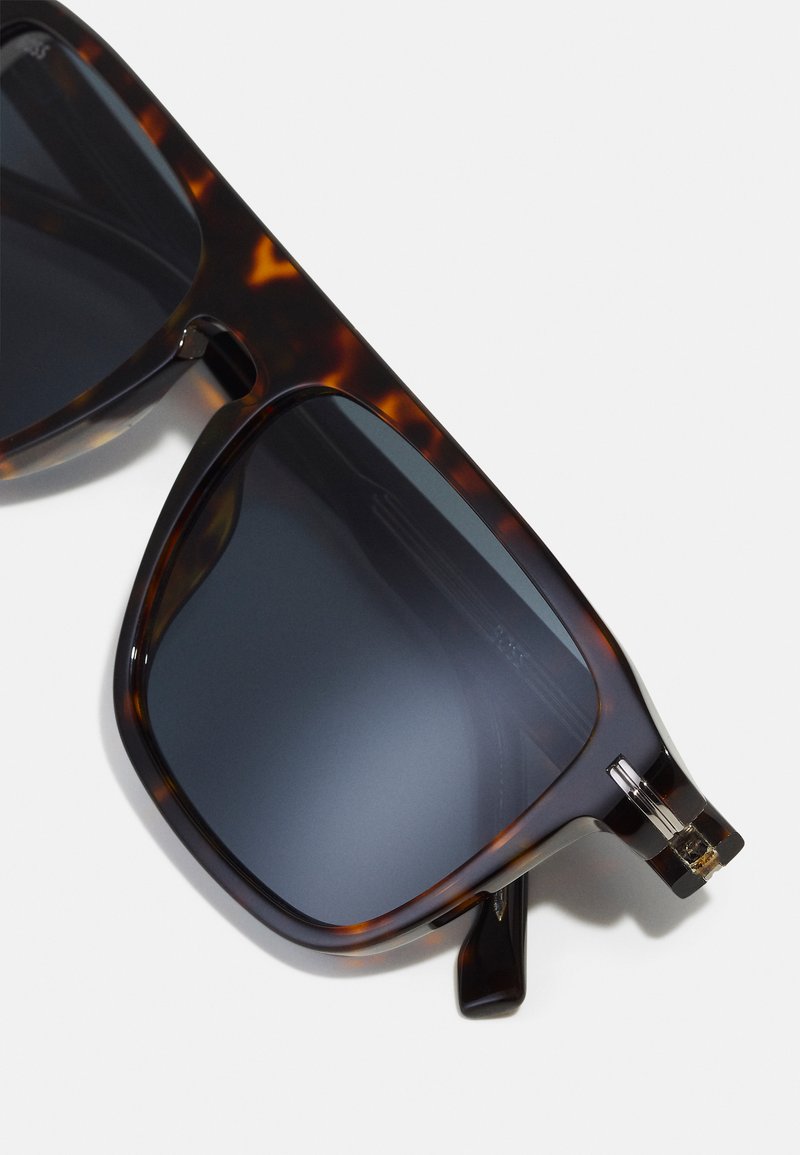 Occhiali da sole tartarugati con lenti scure, design a forma quadrata, dettagli in metallo lucido e terminali a coste per una presa migliore.